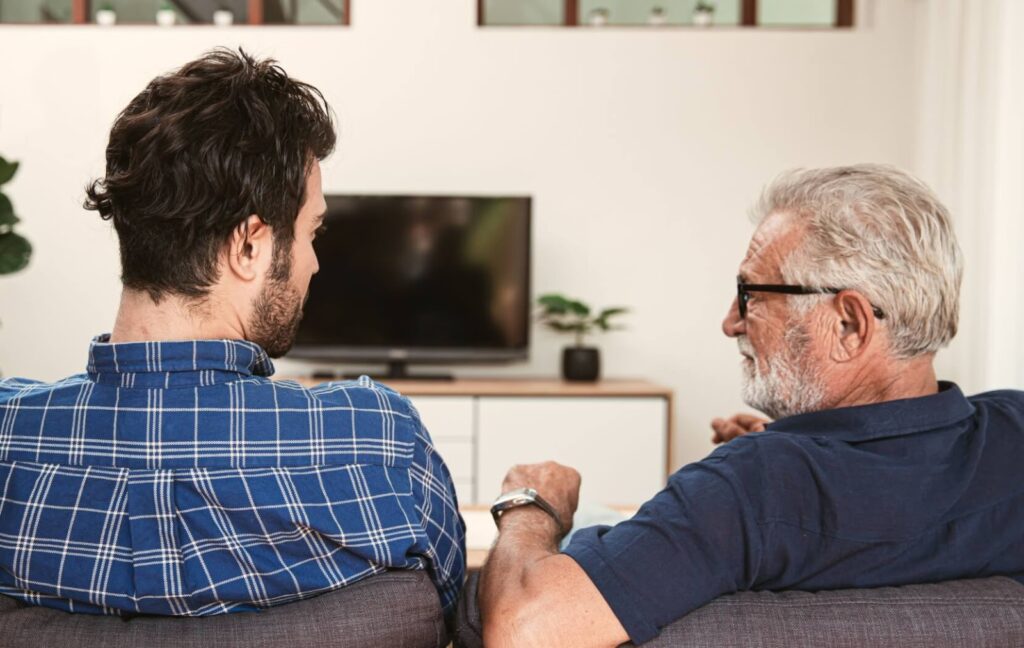 A senior and their adult child sit side by side on a couch. The are discussing the senior's struggles and if it is time for assisted living.