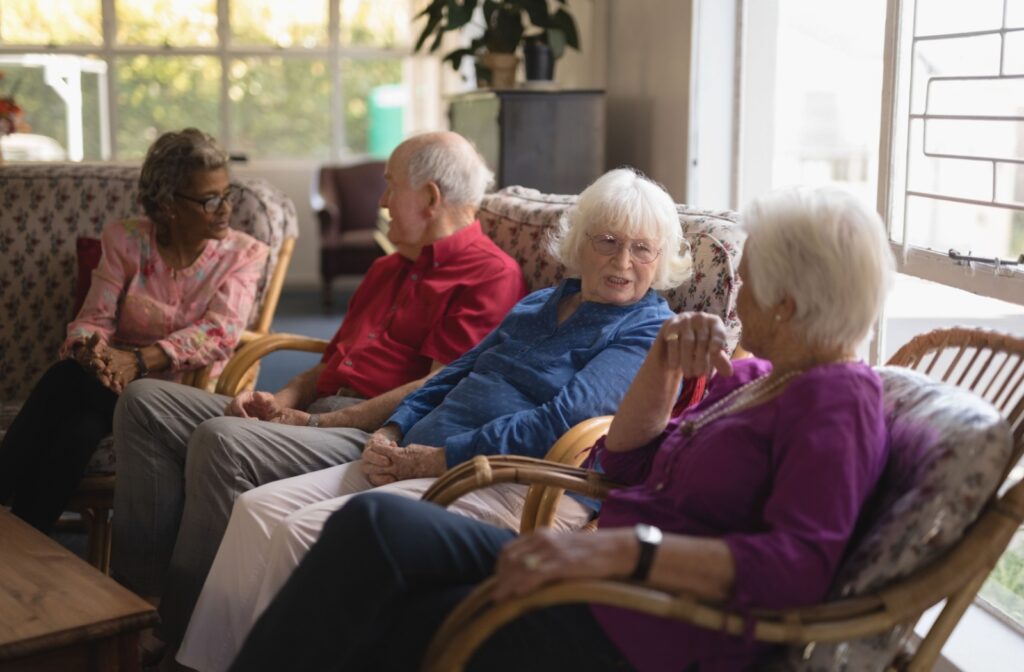 A group of seniors sits on comfortable chairs in their assisted living community for an afternoon chat.