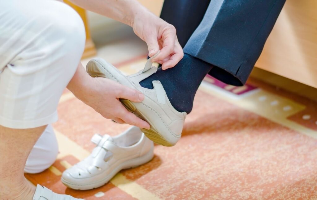 A staff member helps a resident with limited mobility strap on their shoes in the morning before heading to breakfast.