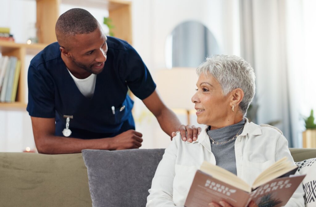 A caregiver checking in on a resident while they read a book in assisted living.
