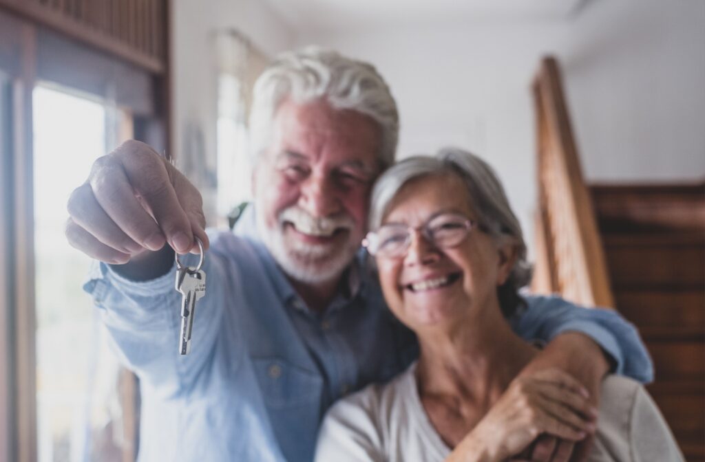 A happy senior couple embrace while holding out a set of keys to their new retirement home